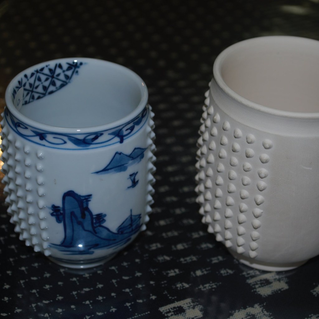 A teacup on the right is before placing in a kiln. It is four times larger than the finished product on the left.
